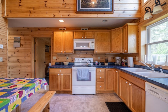 kitchen featuring dark countertops, light tile patterned flooring, a sink, wooden walls, and white appliances