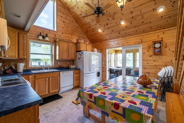 kitchen featuring dark countertops, washer / clothes dryer, a sink, wood walls, and white appliances