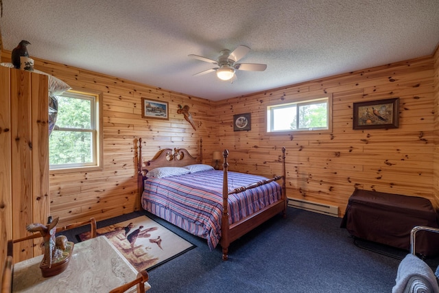 carpeted bedroom with a baseboard heating unit, multiple windows, and a textured ceiling