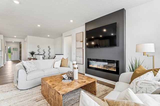 living area with baseboards, wood finished floors, a glass covered fireplace, and recessed lighting