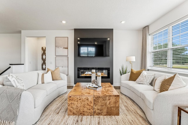 living room with a textured ceiling, baseboards, a glass covered fireplace, and recessed lighting