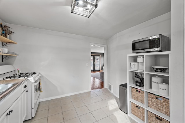 kitchen featuring light tile patterned floors, open shelves, stainless steel microwave, white cabinets, and white range with gas stovetop