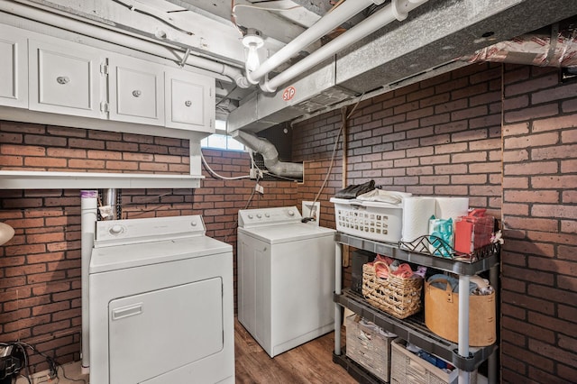 laundry area with light wood-type flooring, cabinet space, brick wall, and washing machine and dryer