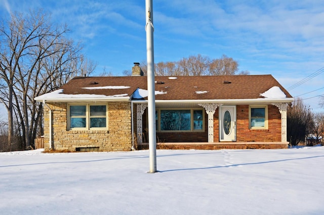 ranch-style home featuring stone siding, roof with shingles, and a chimney