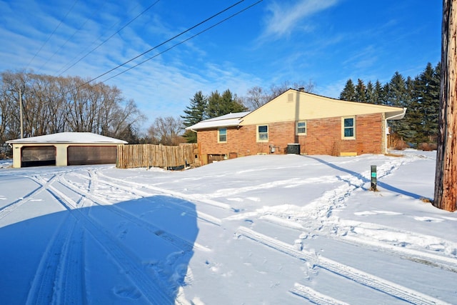 yard layered in snow featuring a garage, cooling unit, fence, and an outbuilding