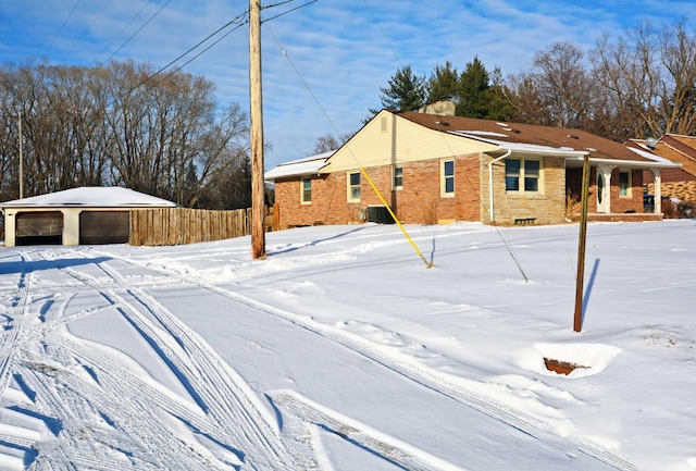 snow covered property featuring a garage, brick siding, and fence