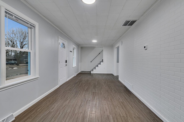 foyer featuring brick wall, stairs, visible vents, and dark wood finished floors