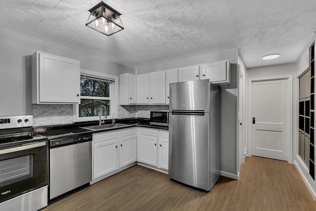 kitchen featuring appliances with stainless steel finishes, dark countertops, a sink, and white cabinetry