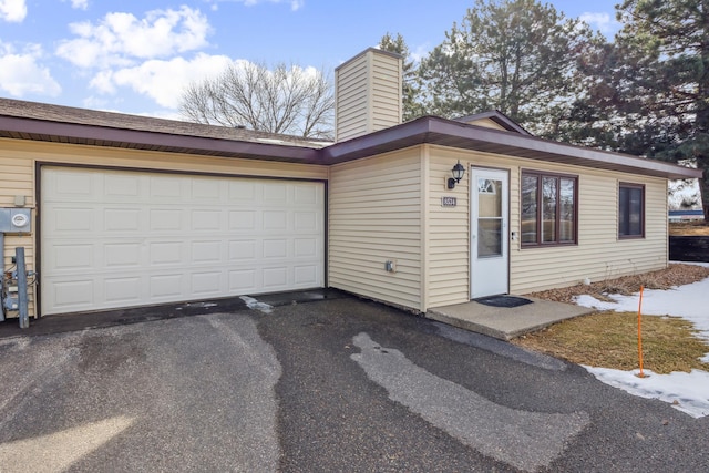 ranch-style home featuring an attached garage, a chimney, and driveway