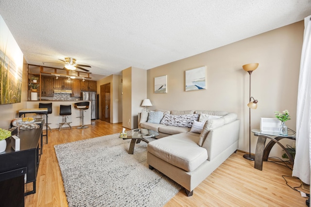 living area featuring a textured ceiling, a ceiling fan, and light wood finished floors