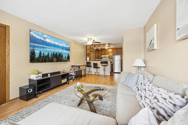 living area featuring light wood finished floors, baseboards, a textured ceiling, and ceiling fan