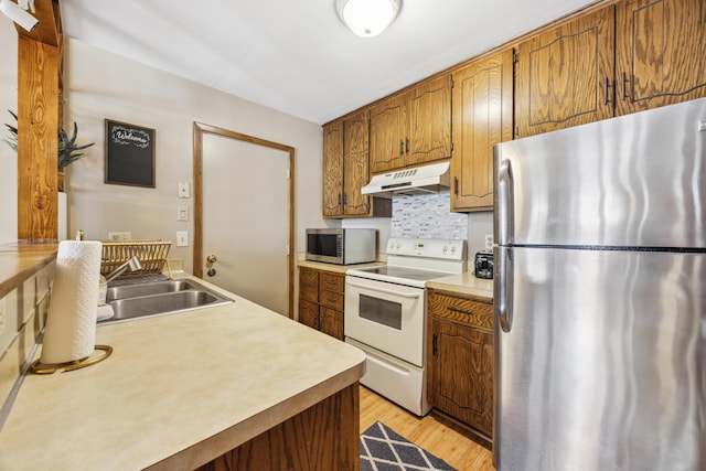 kitchen with a sink, stainless steel appliances, light countertops, light wood-style floors, and under cabinet range hood