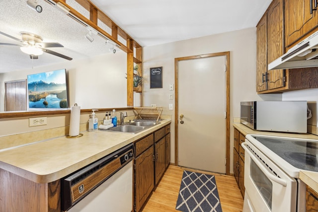 kitchen with light wood-type flooring, under cabinet range hood, a sink, white appliances, and light countertops