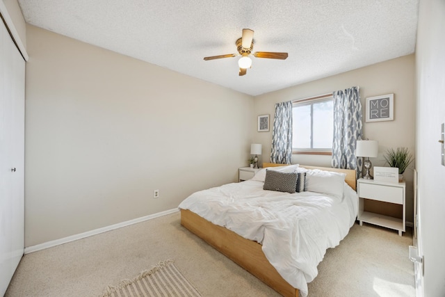 bedroom with a textured ceiling, baseboards, ceiling fan, a closet, and light carpet