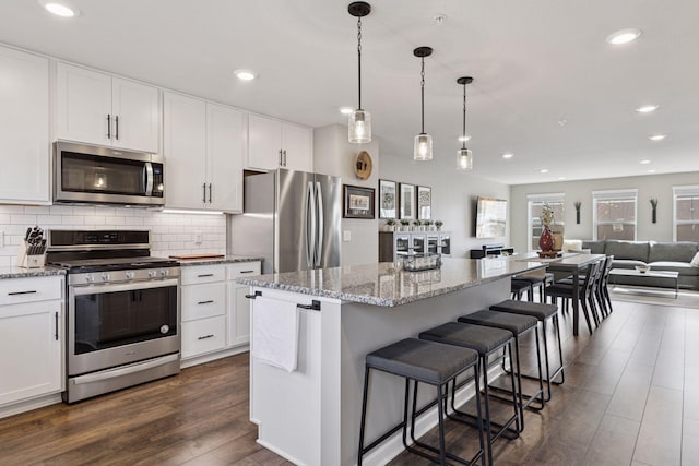 kitchen with decorative backsplash, open floor plan, appliances with stainless steel finishes, and dark wood finished floors