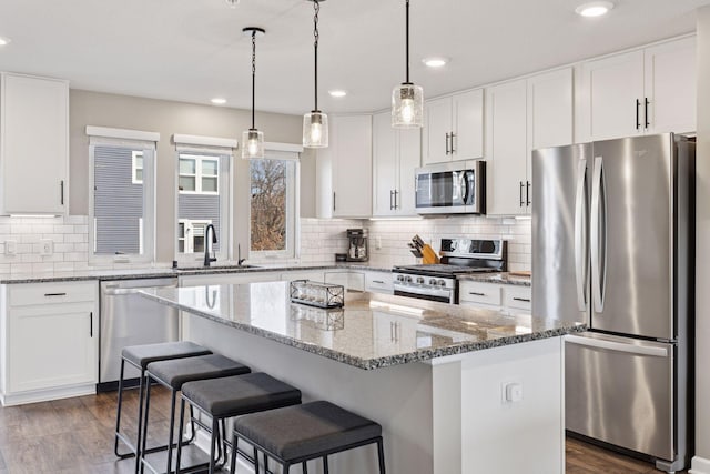 kitchen featuring a sink, a center island, white cabinetry, stainless steel appliances, and light stone countertops