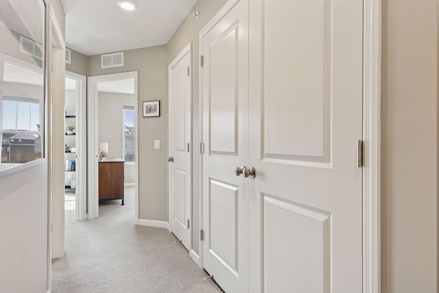 hallway featuring visible vents, light colored carpet, and baseboards