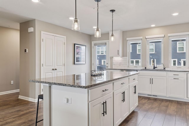 kitchen featuring dark wood finished floors, a kitchen island, tasteful backsplash, and a sink