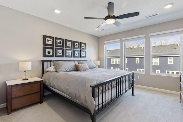 bedroom featuring visible vents, a textured ceiling, baseboards, light colored carpet, and ceiling fan