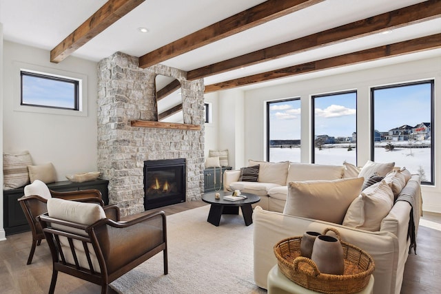 living room with beamed ceiling, wood finished floors, and a stone fireplace