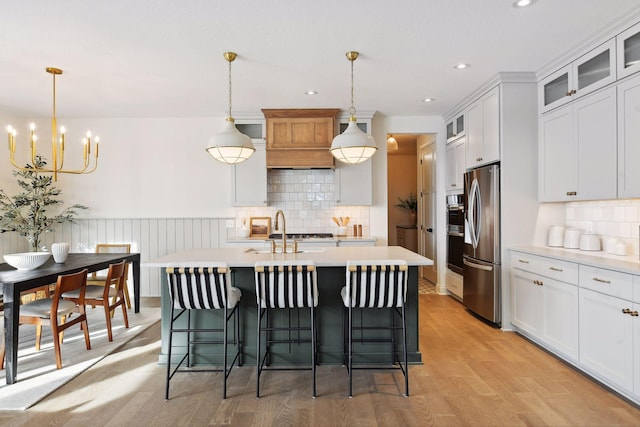 kitchen with light countertops, light wood-style floors, freestanding refrigerator, a sink, and an island with sink