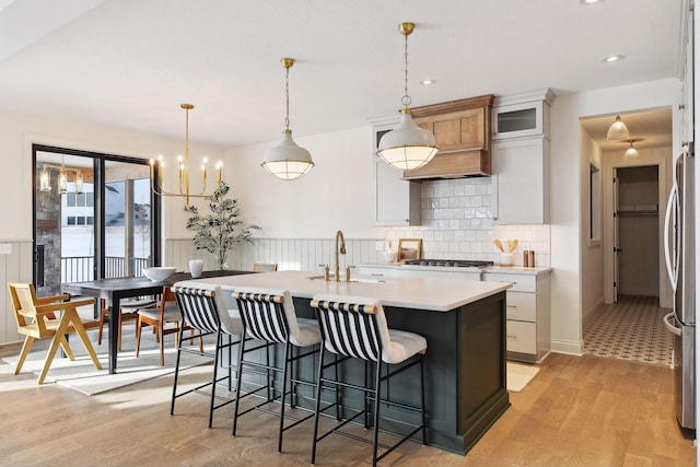 kitchen with a breakfast bar, a sink, light countertops, freestanding refrigerator, and a center island with sink