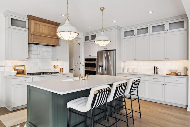 kitchen featuring a center island with sink, stainless steel appliances, light countertops, light wood-style floors, and a sink