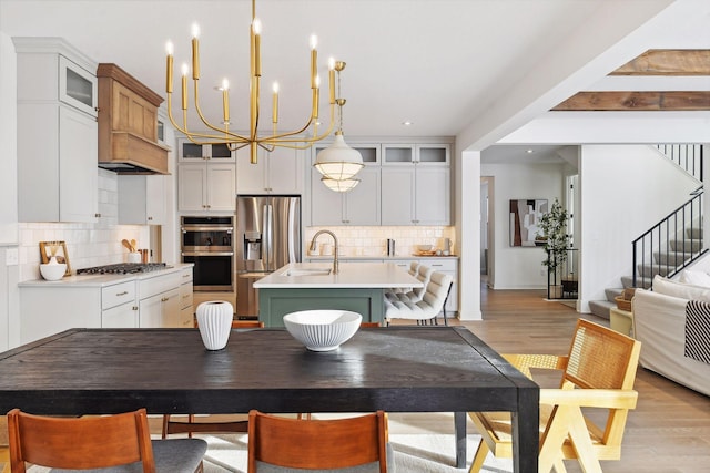 kitchen with stainless steel appliances, light wood-style floors, light countertops, a center island with sink, and pendant lighting