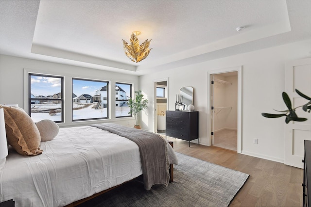 bedroom with a textured ceiling, a tray ceiling, wood finished floors, and baseboards