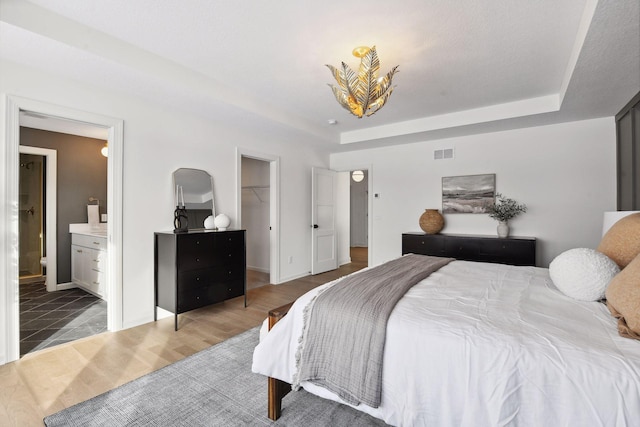 bedroom with a tray ceiling, visible vents, a spacious closet, and wood finished floors