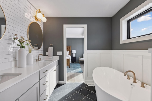 full bath with a sink, wainscoting, a soaking tub, tile patterned floors, and double vanity