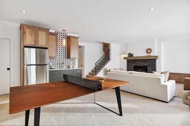 living area with a brick fireplace, recessed lighting, stairway, and light colored carpet