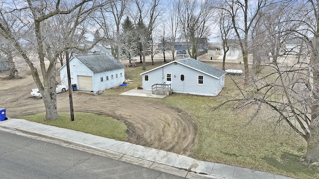 view of front of property with a shingled roof, dirt driveway, a front lawn, and an outbuilding