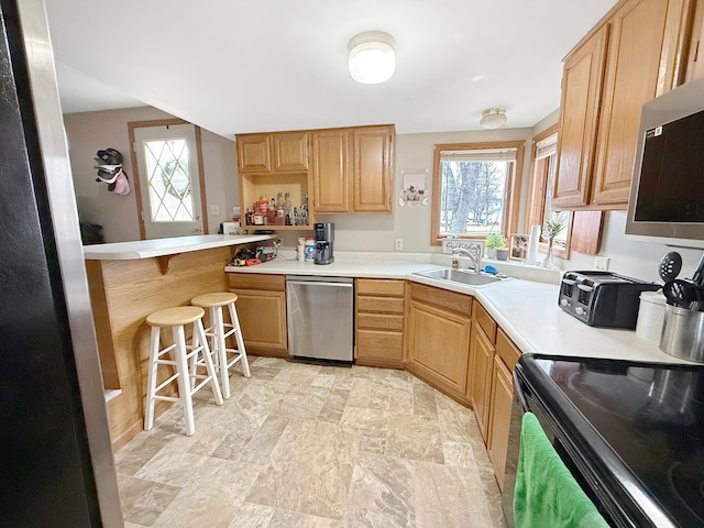 kitchen with light countertops, light brown cabinetry, appliances with stainless steel finishes, a sink, and a kitchen breakfast bar