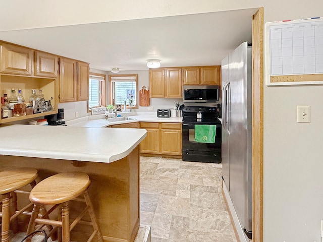 kitchen featuring a breakfast bar area, light countertops, appliances with stainless steel finishes, a sink, and a peninsula