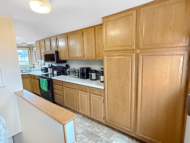 kitchen featuring black range with electric stovetop, a sink, light countertops, light brown cabinetry, and stainless steel microwave