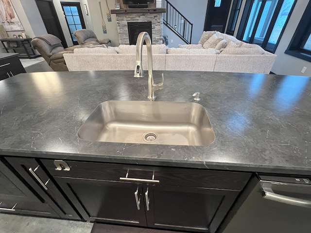 interior details with dark countertops, a stone fireplace, dark cabinets, and a sink