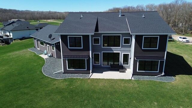 rear view of house with a patio, board and batten siding, roof with shingles, and a lawn