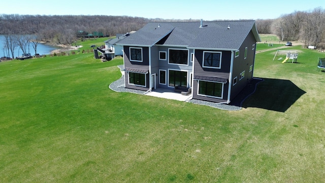 rear view of property with a lawn, a water view, roof with shingles, and a patio area