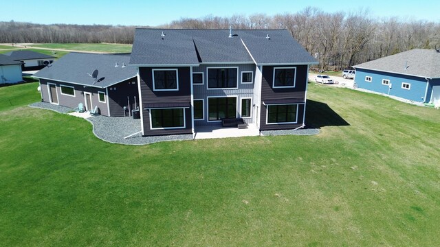 rear view of property featuring a shingled roof, a patio area, and a yard