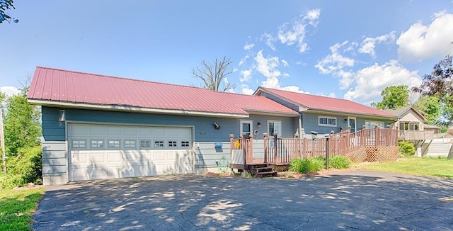 single story home featuring metal roof, a garage, a deck, and aphalt driveway