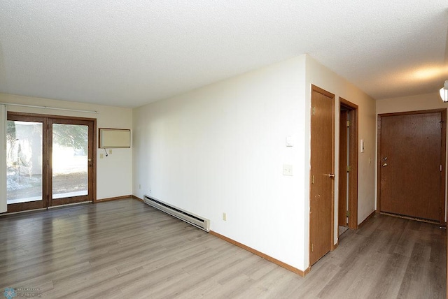 empty room featuring a textured ceiling, a baseboard radiator, wood finished floors, and baseboards