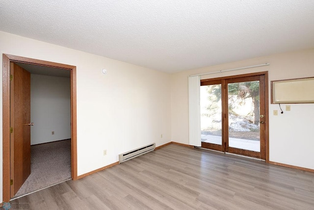 spare room featuring light wood-style floors, baseboards, baseboard heating, and a textured ceiling