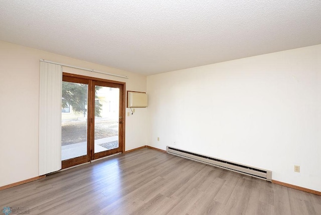 spare room featuring a textured ceiling, baseboard heating, wood finished floors, and baseboards