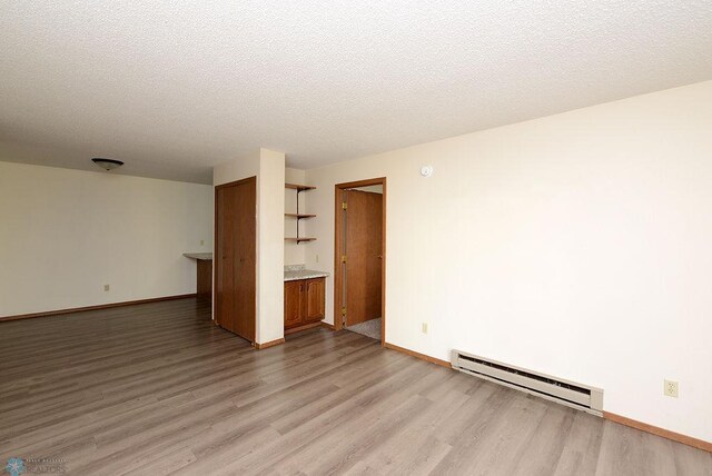 unfurnished room featuring a textured ceiling, baseboard heating, light wood-type flooring, and baseboards