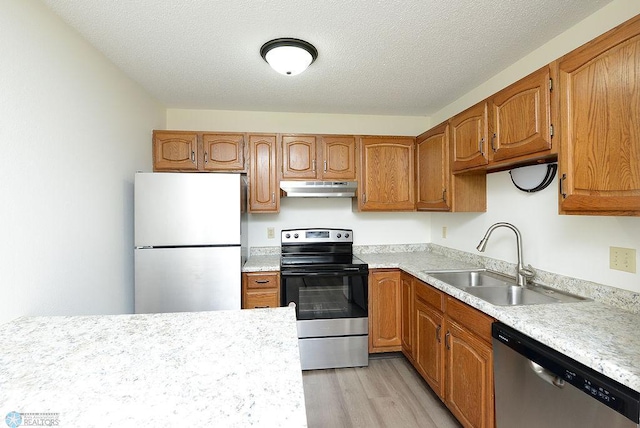 kitchen with light countertops, appliances with stainless steel finishes, a sink, light wood-type flooring, and under cabinet range hood