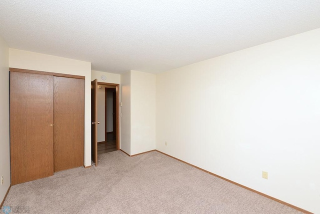 unfurnished bedroom featuring a closet, light carpet, a textured ceiling, and baseboards