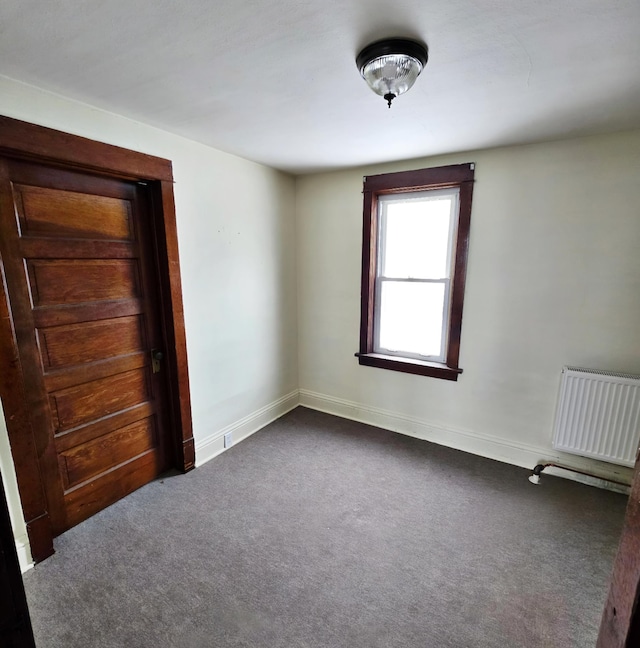 unfurnished bedroom with radiator heating unit, dark carpet, and baseboards