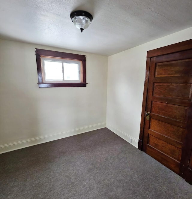 empty room with a textured ceiling, dark colored carpet, and baseboards