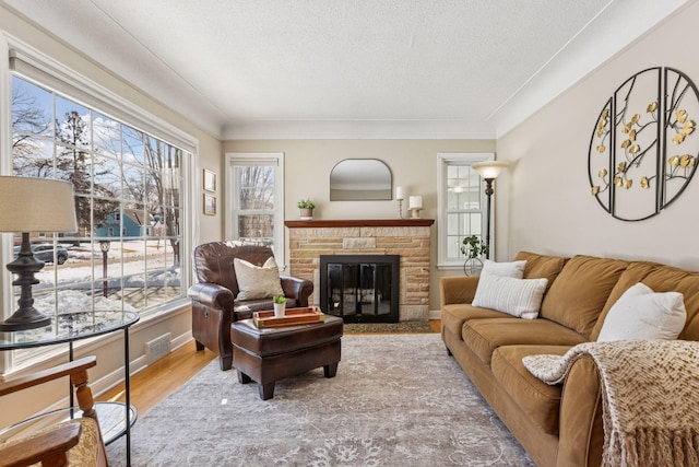 living room featuring a glass covered fireplace, plenty of natural light, a textured ceiling, and light wood-style flooring